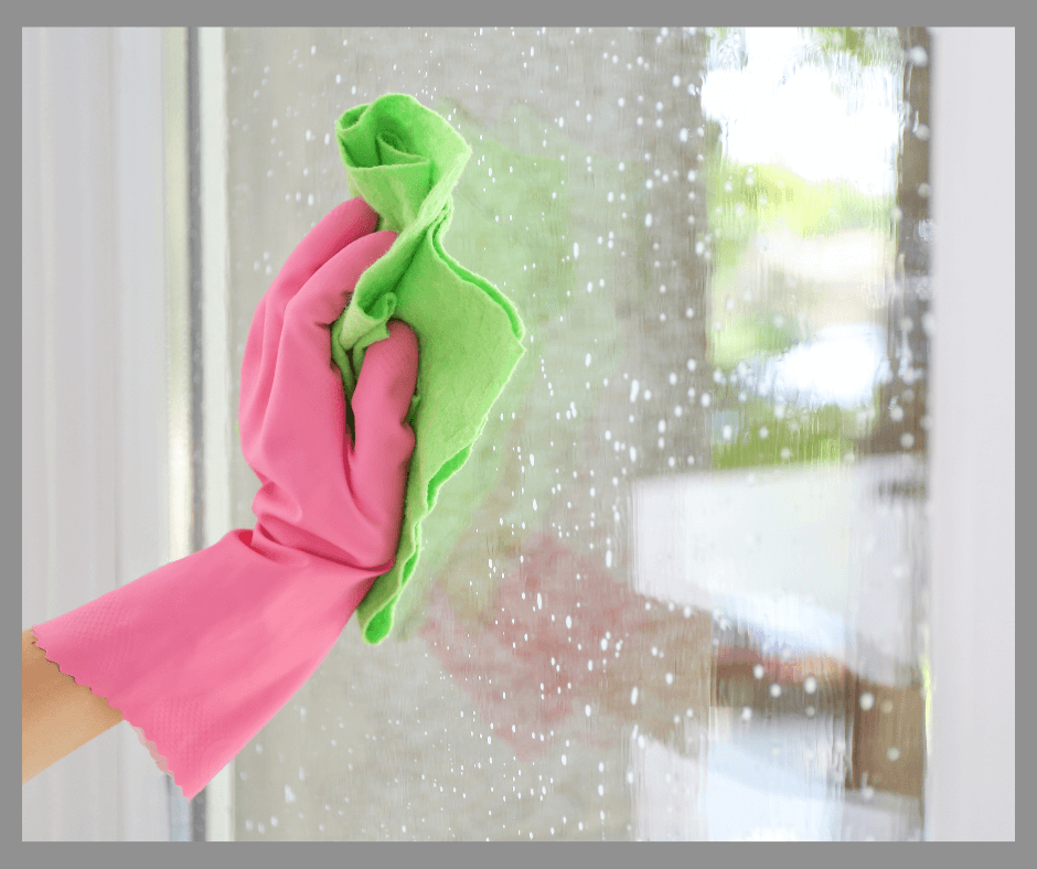 A hand in a pink glove washing a window.